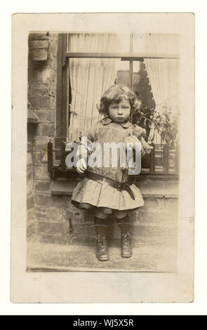 Primi del novecento cartolina del bambino tenendo un orsacchiotto fuori casa, con caduta in casa abito di cintura con un orsacchiotto, fuori casa, con caduta in casa abito di cintura con cinghia, circa 1907, U.K. Foto Stock