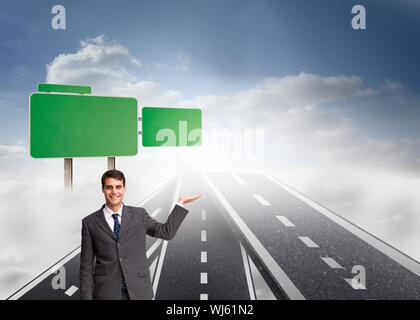 Immagine composita di happy businessman presentando nuove strade con verde cartelli stradali nel cielo Foto Stock