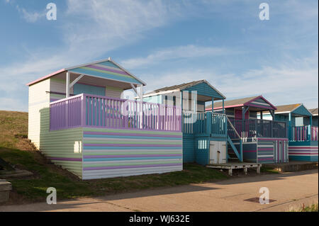 Righe colorate di cabine sulla spiaggia, dipinte e accuditi presso sunrise intavolato pronto per un successivo impiego su estati calde giorno a Whitstable lungomare, Tankerton Foto Stock