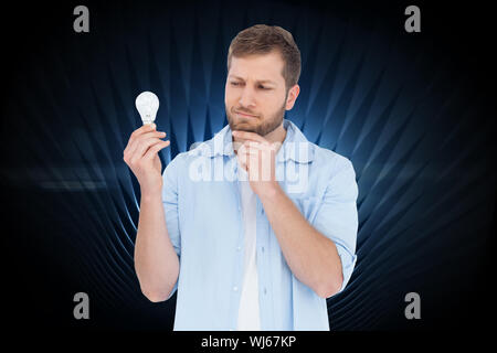 Immagine composita del modello scettico su sfondo bianco in possesso di una lampadina Foto Stock