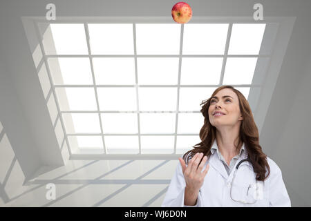 Immagine composita di felice brunette medico gettando apple Foto Stock