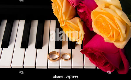 Mazzo di rose giacente sul piano con gli anelli di nozze. Giallo e rose rosse regalo di nozze con le fedi. Preparazione per un matrimonio o di San Valentino d Foto Stock