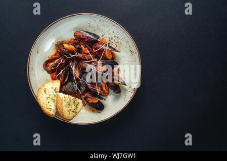 Piatti con le cozze in una piastra su uno sfondo nero. vista da sopra. copyspace. il pesce. Foto Stock