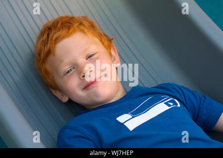 Ragazzo disteso sul pavimento. Ritratto di ragazzo europeo con gli occhi verdi, guardando direttamente alla fotocamera. Vista aerea. Funny bambino con lo zenzero ricci Foto Stock