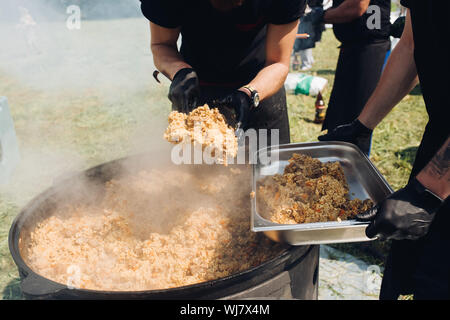 Gli uomini di mettere pilaf dal calderone nel contenitore. Foto Stock