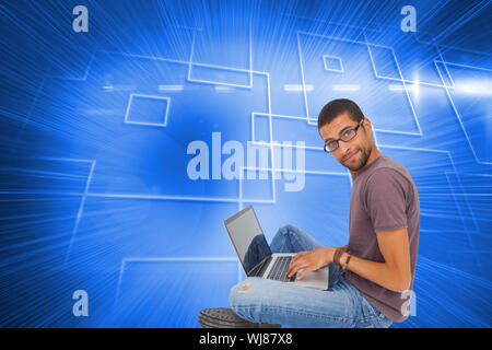 Immagine composita dell'uomo con gli occhiali seduto sul pavimento con il laptop e guardando la fotocamera Foto Stock