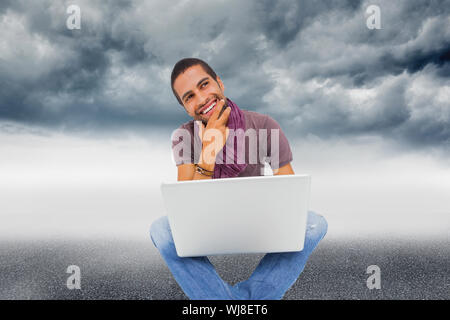 Immagine composita di pensare uomo seduto sul pavimento con il laptop e sorridente Foto Stock