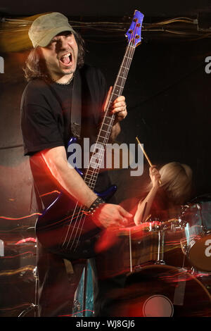 Bass Player giocando su un palco con il batterista femmina. Girato con lampeggiatori stroboscopici e rallentare la velocità dello shutter per creare atmosfera di illuminazione e gli effetti di sfocatura. Motion bl Foto Stock