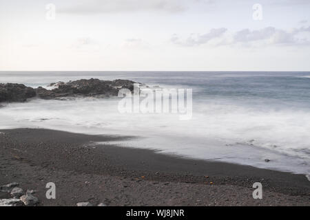 Mesa del mar spiaggia vulcanica di sabbia e rocce, fotografie con lunghi tempi di esposizione, con l'Oceano Atlantico onde, orizzonte con la luce del tramonto, Tacoronte, Tenerife, Cana Foto Stock