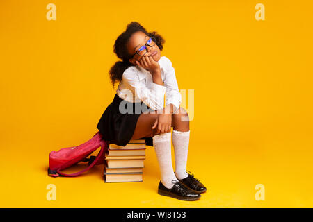 Annoiato Schoolgirl seduti sulla pila di libri su sfondo giallo Foto Stock
