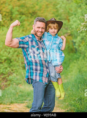 Forte il padre e il figlio nel cappello da cowboy sul ranch. kid in stivali di gomma. uomo felice papà nella foresta. natura e uomo. il giorno della famiglia. felice giornata della terra. Eco farm. piccolo ragazzo aiutare il padre in agricoltura. forti legami. Foto Stock