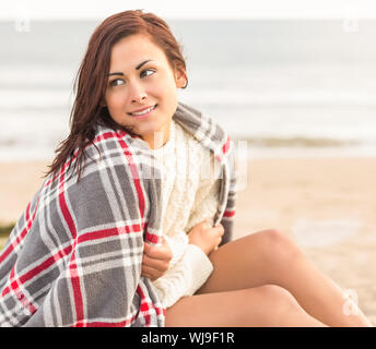 Bella giovane donna copertura lei stessa con coperta in spiaggia Foto Stock