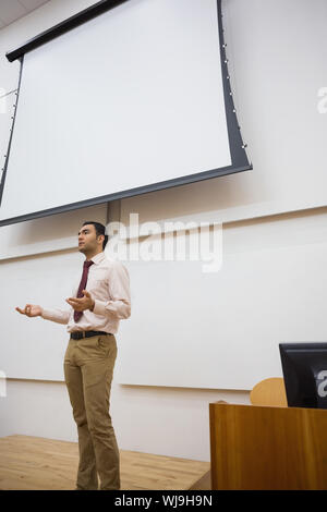 Elegante insegnante maschio in piedi contro lo schermo di proiezione in sala Foto Stock