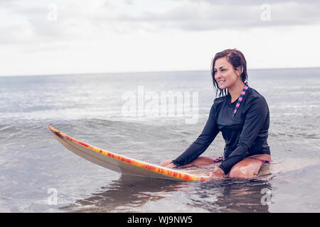 Bella giovane donna seduta sulla tavola da surf in acqua in spiaggia Foto Stock