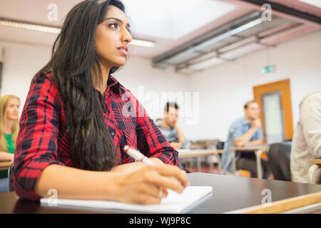 Giovane studentessa con altri scrivere appunti in classe Foto Stock