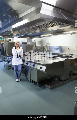 Giovani chef felice in piedi accanto alla superficie di lavoro in cucina professionale Foto Stock