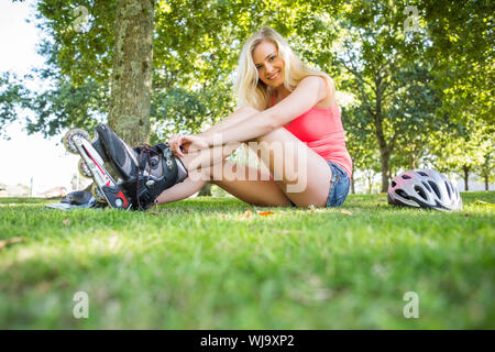 Casual bionda sorridente mettendo sul rullo di pale in un parco in una giornata di sole Foto Stock