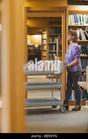 Femmina gravi bibliotecario spingendo un carrello in una libreria Foto Stock