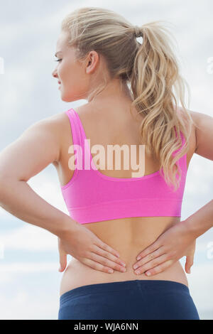 Vista posteriore di una donna sana nel reggiseno per lo sport che soffrono di dolori alla schiena sulla spiaggia Foto Stock