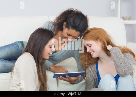 Giovani femmine amici utilizzando la tavoletta digitale insieme sul divano di casa Foto Stock