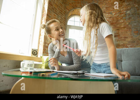 Femmina insegnante caucasica e bambina, o la mamma e figlia. Homeschooling. Seduti sul divano e disegno con vernici, scrittura, conversazione e divertirsi. Istruzione, scuola, studiando concetto. Foto Stock