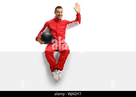 A piena lunghezza Ritratto di una giovane racer in un uniforme rosso seduto su un pannello e agitando isolati su sfondo bianco Foto Stock