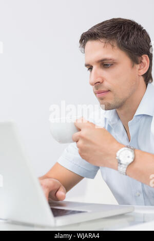 Uomo serio con tazzina utilizzando portatile a casa Foto Stock