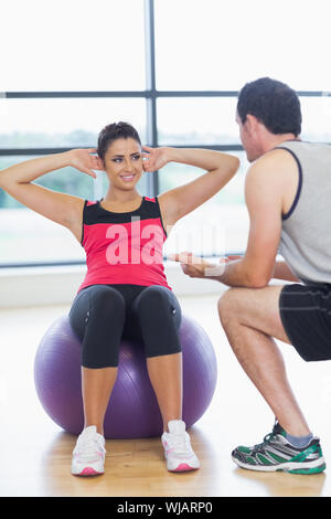 Trainer aiutando la donna non sgranocchia addominale sulla sfera di fitness Foto Stock