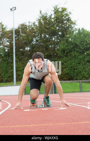 Giovane uomo pronto a correre su una pista per la corsa Foto Stock