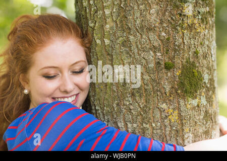 Sorridente redhead abbracciando un albero Foto Stock