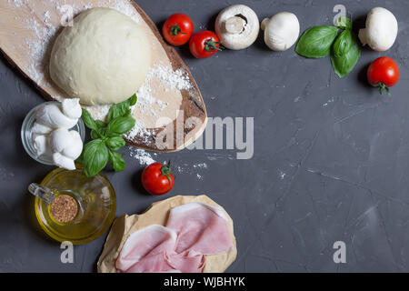 Pizza crudo ingredienti sul cartone grigio con copia spazio su Centro. È possibile mettere la vostra immagine o iscrizione al centro, pasta, pomodori, funghi Foto Stock