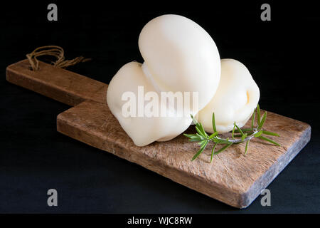 Fresco italiano meridionale tradizionale Scamorza semi-soft formaggio di vacca su uno sfondo nero, pronto a mangiare, vicino. La scamorza è molto popolare di formaggio in P Foto Stock