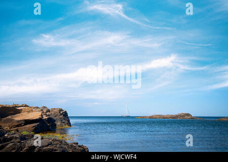 Barca a vela sul mare sotto un cielo blu con scogliere in riva al mare in estate Foto Stock