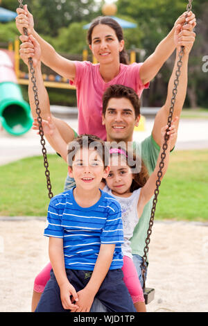 Jolly famiglia caucasica oscillanti in parco all'aperto Foto Stock