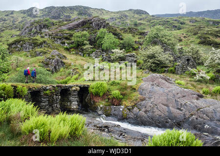 Due persone che camminano su lastra di pietra ponte Afon Lledr a rovinato insediamento di Cwm-fynhadog-uchaf su pendii di Moel Lledr. Dolwyddelan Wales UK Foto Stock