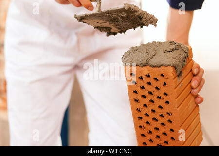 Muratore con mattone sul sito in costruzione Foto Stock