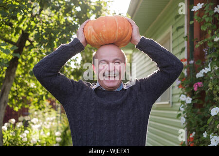 Senior felice uomo ispanico tenendo una zucca in mani. Scegliere una zucca di Halloween nel giardino. Foto Stock