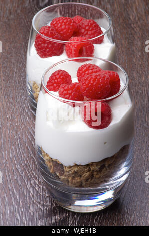 Deliziosi Dessert con fresche Lamponi maturi, muesli e panna in due bicchieri in una fila closeup su sfondo di legno Foto Stock