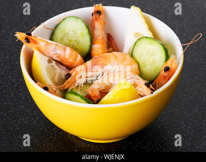 Gamberetti freschi in una ciotola con i limoni e il cetriolo. Su tavolo da cucina. Foto Stock