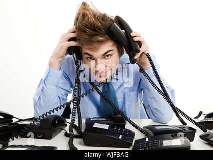 Giovane uomo seduto in ufficio e rispondere a più telefoni contemporaneamente Foto Stock