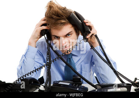 Giovane uomo seduto in ufficio e rispondere a più telefoni contemporaneamente Foto Stock