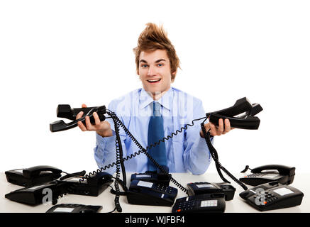 Giovane uomo seduto in ufficio e rispondere a più telefoni contemporaneamente Foto Stock