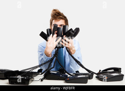 Giovane uomo in ufficio e rispondere a più telefoni contemporaneamente Foto Stock