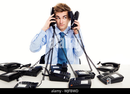 Giovane uomo in ufficio e rispondere a più telefoni contemporaneamente Foto Stock