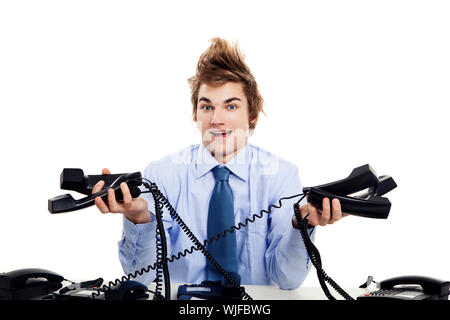 Giovane uomo seduto in ufficio e rispondere a più telefoni contemporaneamente Foto Stock