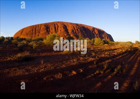 Uluru. Un monolito di Uluru all'aumento in arancio luminoso raggi del sole, lunghe ombre. Foto Stock