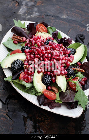 Una sana insalata con melograno, avocado, pomodori, mandorle e lattuga argula oltre un rustico sfondo. Foto Stock