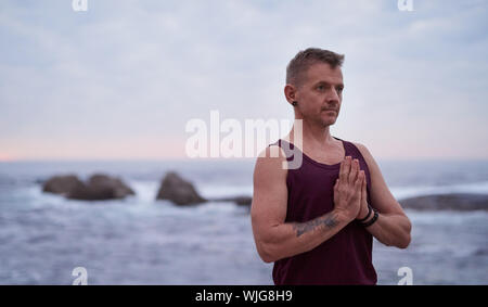 L'uomo meditando durante la pratica dello yoga dall'oceano al tramonto Foto Stock