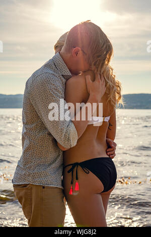 Giovane ragazza abbracciando in piedi in spiaggia contro il sole Foto Stock