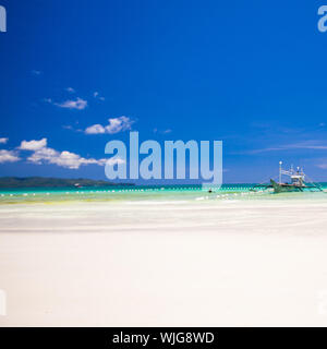 Una perfetta spiaggia sabbiosa tropicale con acque turchesi e piccole barche a vela Foto Stock